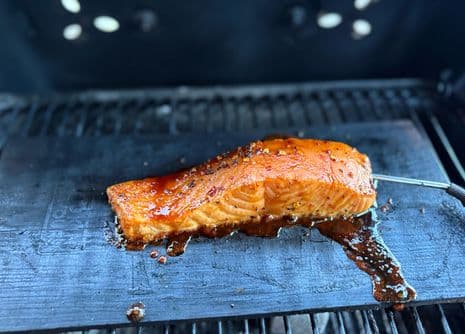 Zalmfilet geglaceerd met saus, bestrooid met kruiden, gerookt op een barbecue op een cederhouten plank, met een vleesthermometer erin.
