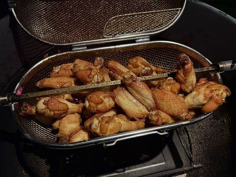 Goudbruine kippenvleugeltjes in een spitmand op een barbecue