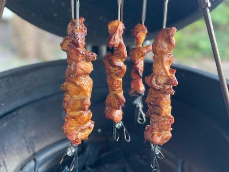 4 spiezen met kip hangend in een kamado barbecue boven hete kolen