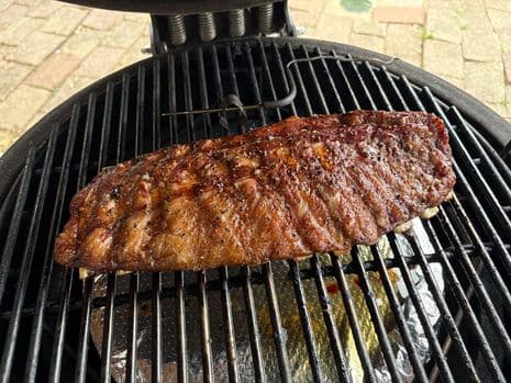 Een rek gerookte Iberico ribbetjes met een knapperig, gekruid korstje op een barbecuerooster.