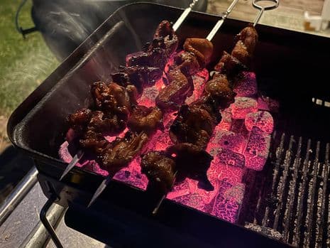 Kipsaté die boven gloeiende kolen op een barbecue liggen te grillen, terwijl de rook opstijgt