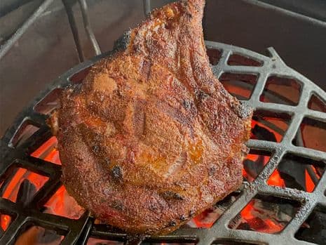 Een gekruide cote de boeuf met grillstrepen die boven gloeiend hete kolen op een gietijzeren rooster wordt gebakken op een barbecue.