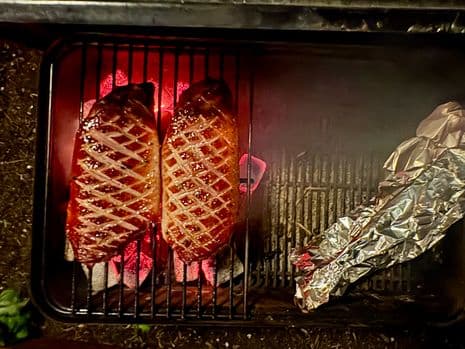 Twee eendenborstfilets boven gloeiende briketten op eeen barbecuerooster