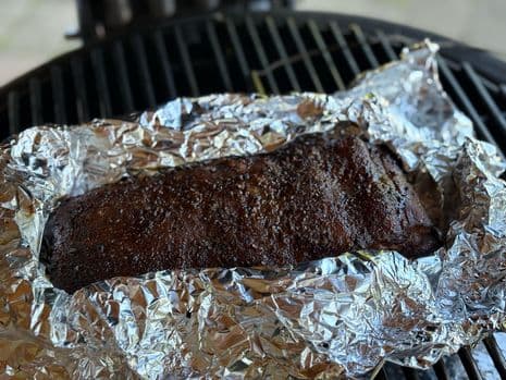 Brisket style buikspek in opgevouwen aluminiumfolie op een barbecue rooster