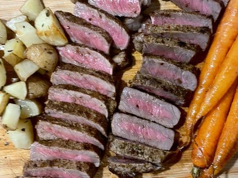 Twee gesneden gegrilde entrecotes met gegrilde wortels en gebakken aardappeltjes
