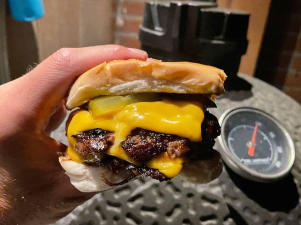 Een smashed onion burger, kaas en augurk op een broodje