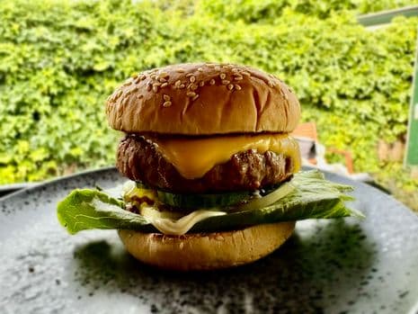 Een cheeseburger met sla, komkommer en saus op een broodje met sesamzaad, op een donker bord