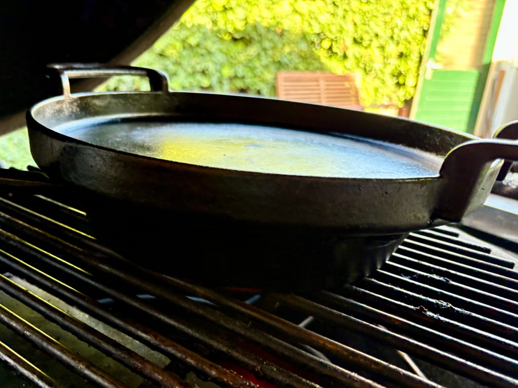 skillet op een barbecue met daarop een andere skillet die als deksel fungeert