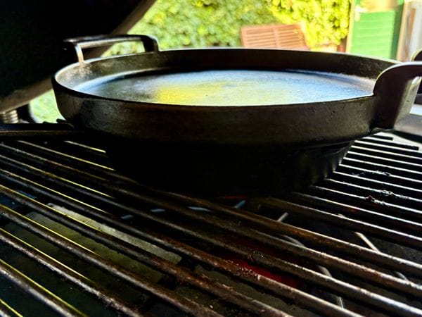 skillet op een barbecue met daarop een andere skillet die als deksel fungeert