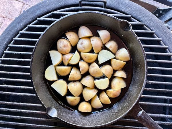 rauwe aardappels liggen in de olie in een skillet op het rooster van een barbecue