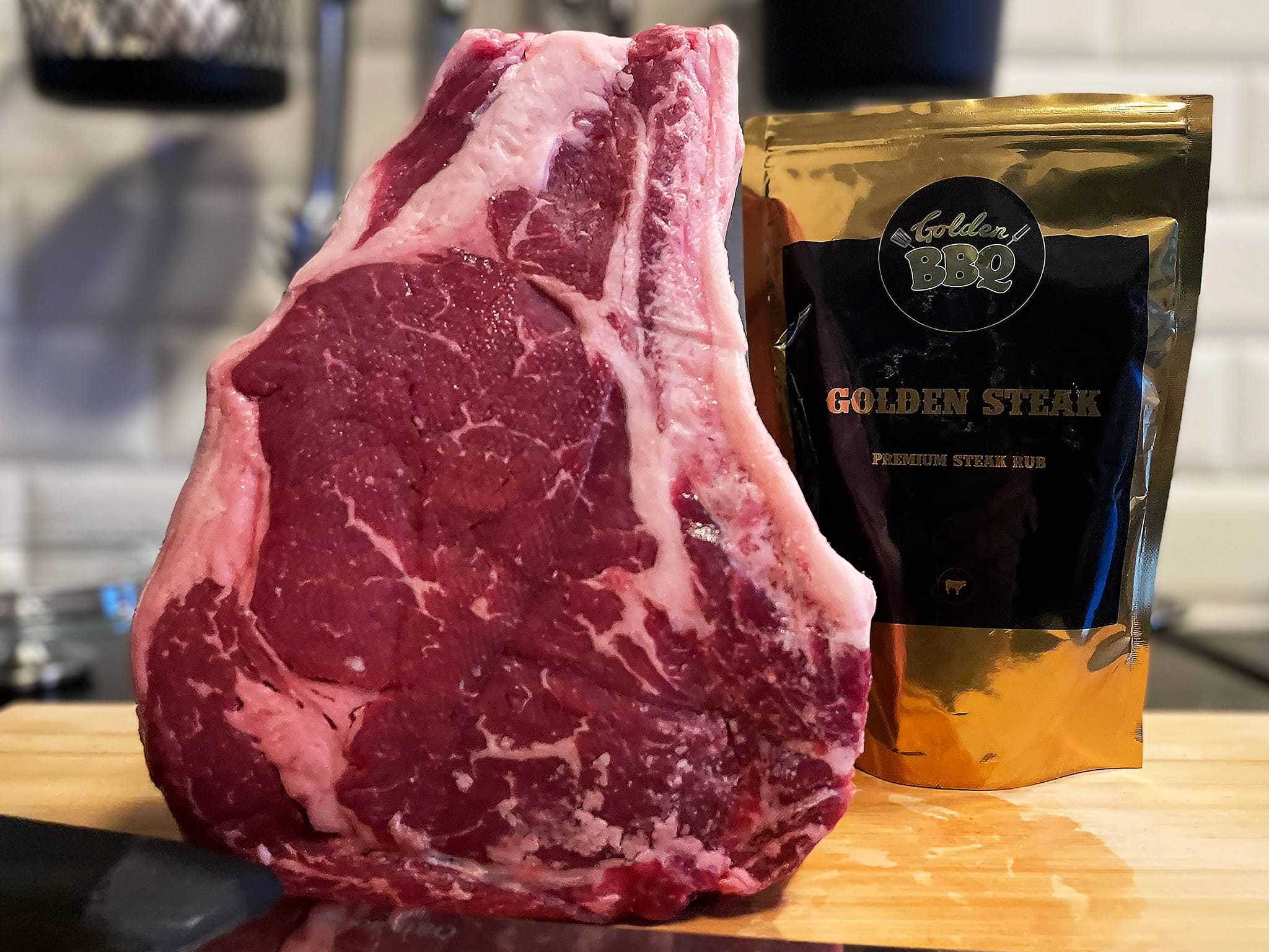 Een rauwe côte de boeuf op een snijplank met een zakje Golden Steak rub op de achtergrond