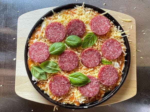 pan pizza in skillet belegd met kaas, salami en basilicum
