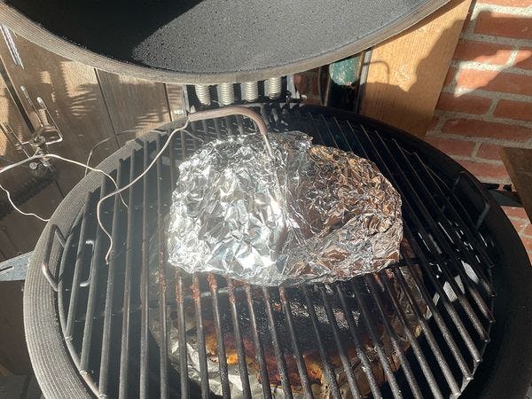 een stuk ingepakte pulled pork in aluminiumfolie op de barbecue met een thermometer er in