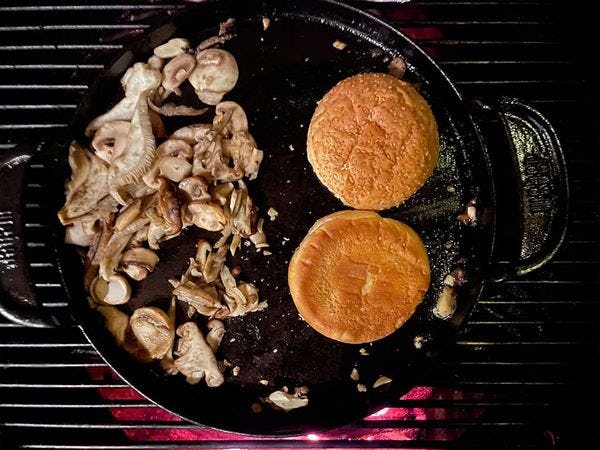 paddestoelen en getoaste hamburger broodjes op een skillet boven het vuur van een barbecue