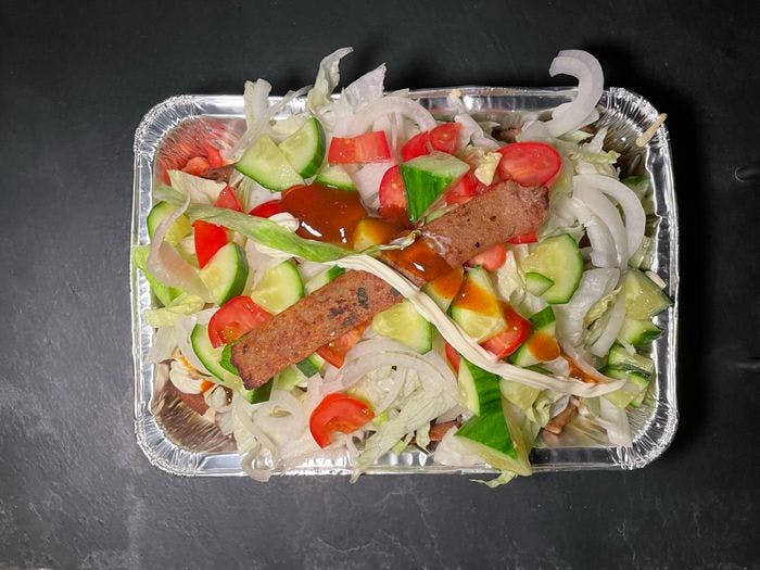 Een kapsalon frikandel speciaal van bovenaf in een aluminiumbakje met salade, mayonaise, currysaus en een stuk frikandel