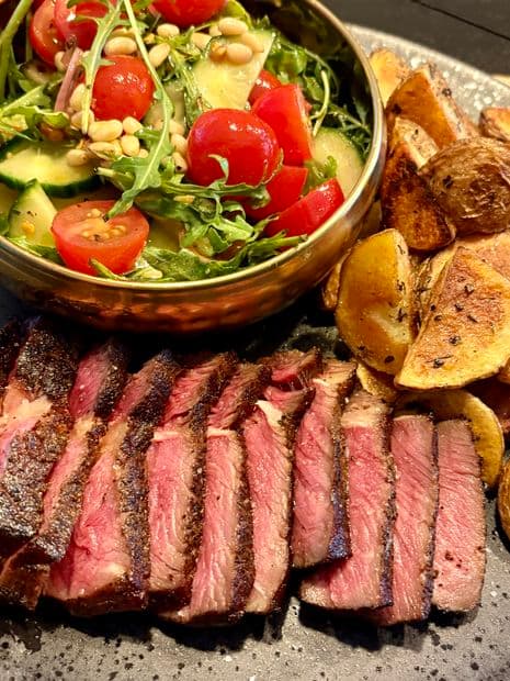 Gesneden medium-rare ribeye met geroosterde aardappeltjes en een verse rucola salade