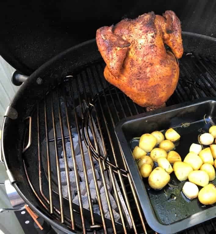 Een beercan chicken en aardappels in een ovenschaal. Indirect op het rooster van een Weber ketelbarbecue